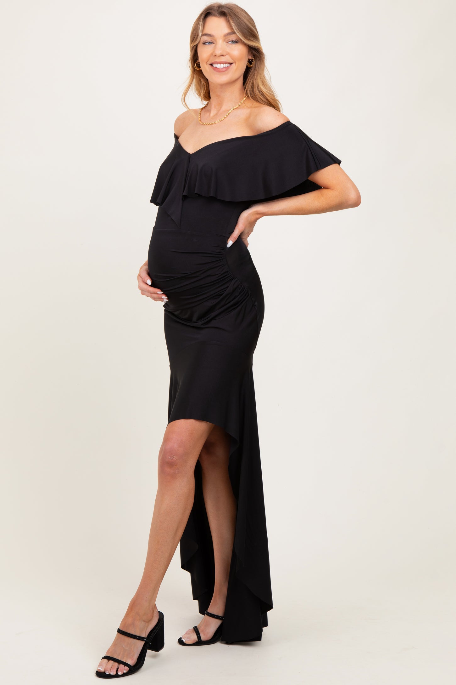 woman wearing a black off-the-shoulder maternity dress with ruffle details and a high-low hem, highlighting her baby bump