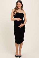 woman wearing a black ruched maternity dress with spaghetti straps and holding her baby bump
