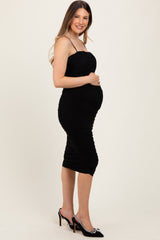 woman wearing a black ruched maternity dress with spaghetti straps and holding her baby bump