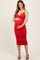 woman wearing a red maternity dress with ruching, holding her baby bump and standing in strappy heels