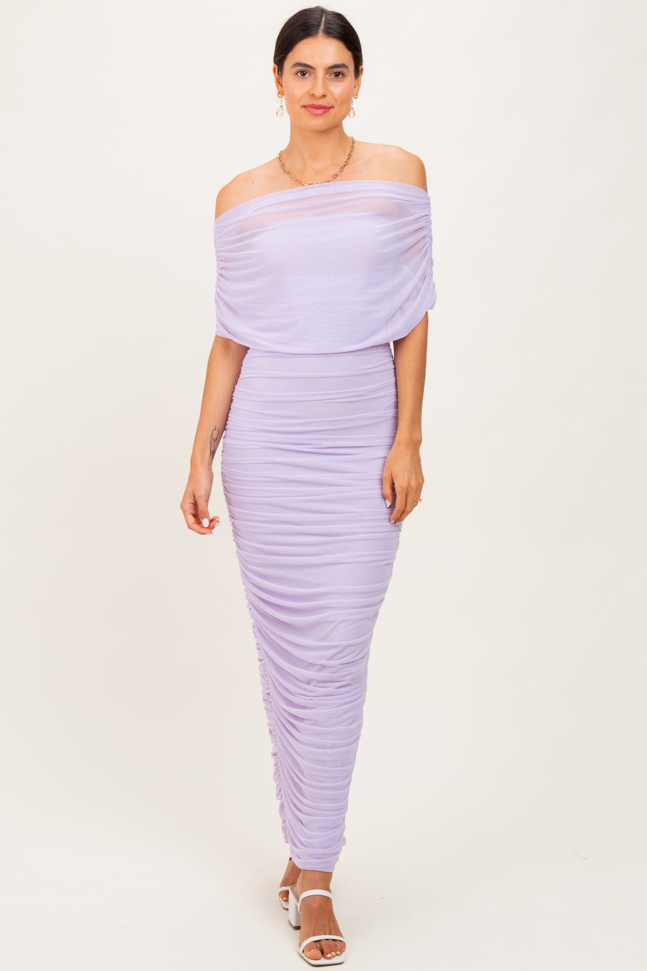 woman wearing a lavender off-the-shoulder ruched dress with a fitted silhouette and a flowing overlay