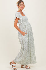 woman wearing a floral maternity maxi dress with ruffled sleeves and a baby bump, standing with hands in pockets