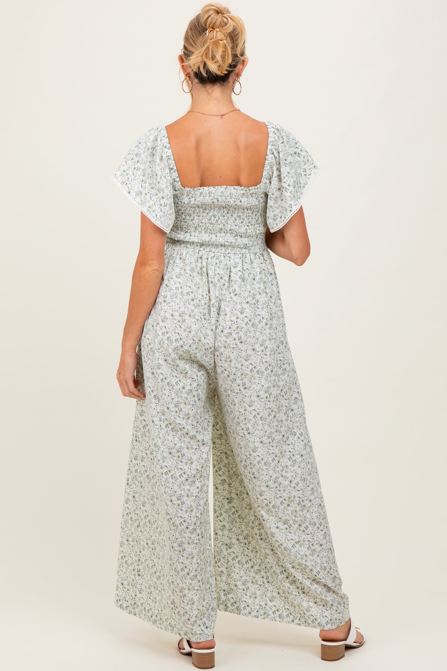 woman wearing a floral maternity jumpsuit with a smocked back and flutter sleeves, showing a baby bump