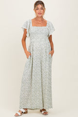 woman wearing a floral maternity maxi dress with a square neck and short flutter sleeves, hands in pockets
