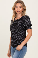 woman wearing a black floral print short sleeve top with a scoop neckline and relaxed fit, paired with blue jeans