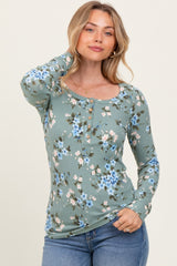 woman wearing a green floral long sleeve top with a scoop neckline and button details, paired with blue jeans