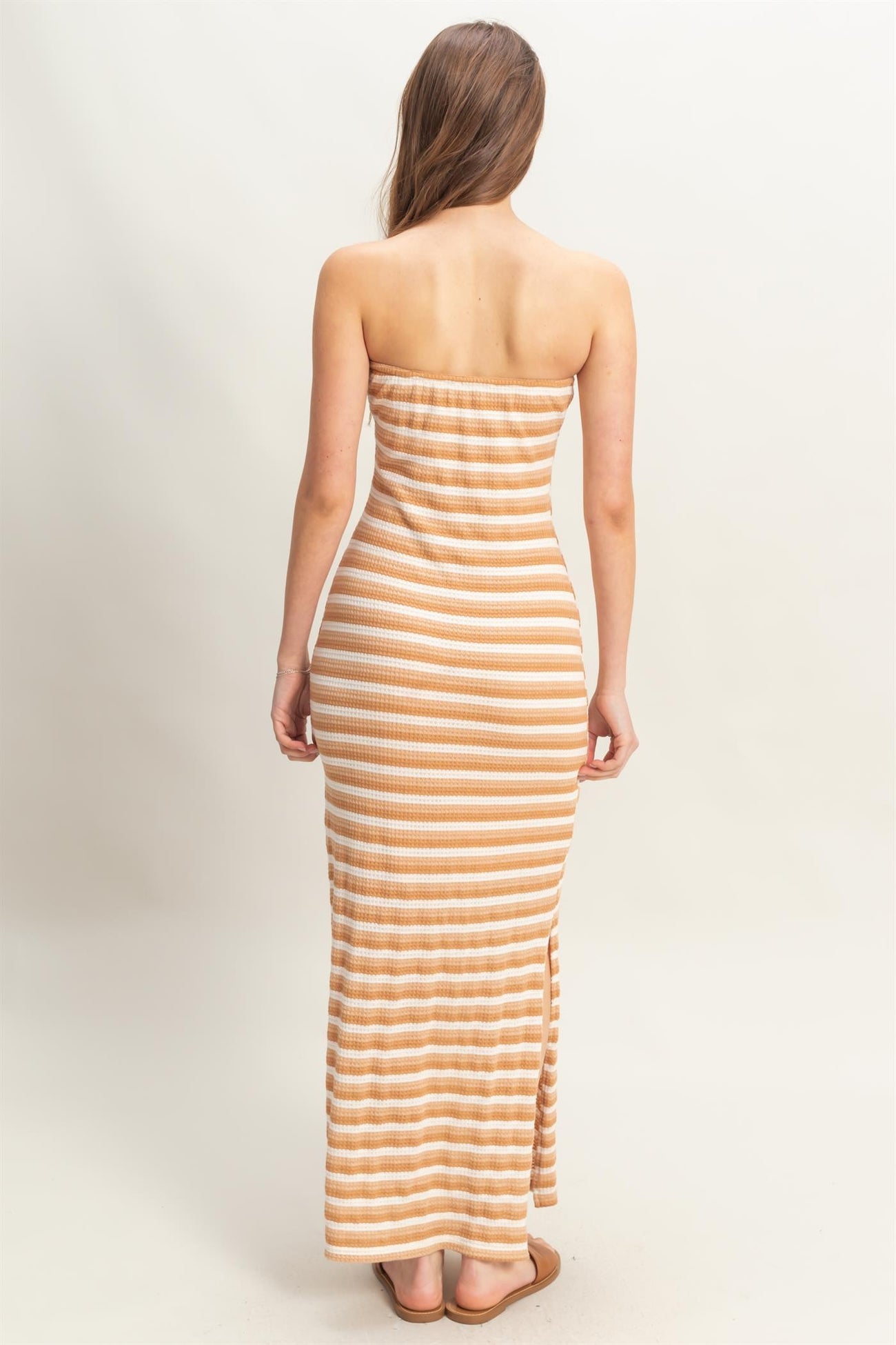 woman wearing a striped strapless maxi dress in orange and cream colors, standing with her back to the camera