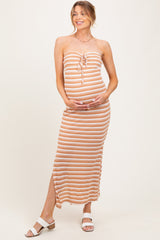 woman wearing a striped maternity maxi dress in peach and white, holding her baby bump and smiling