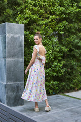 woman wearing a light floral maxi dress with a back tie detail and ruffled sleeves, standing outdoors