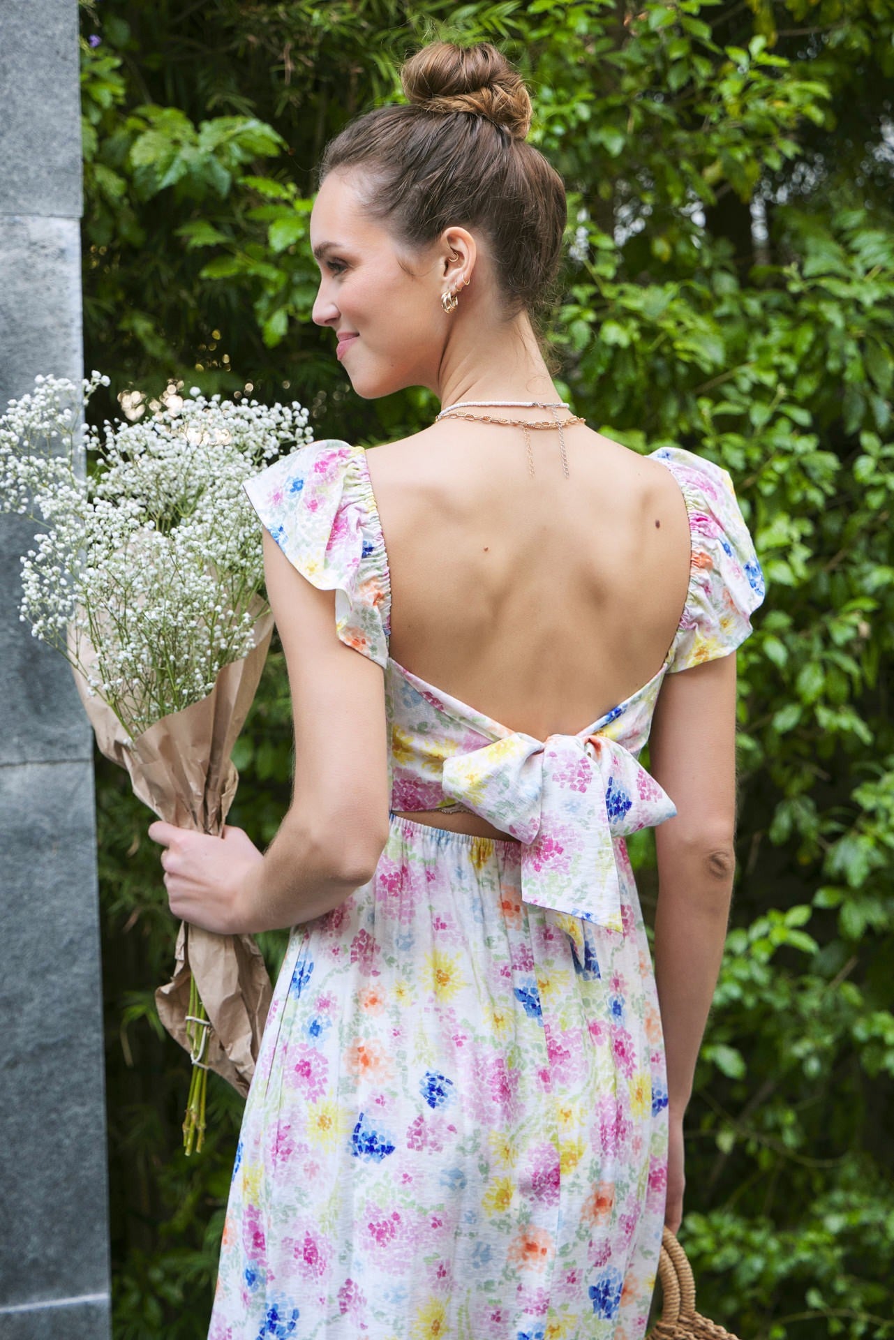 woman wearing a floral backless dress with ruffle sleeves and a bow detail, holding a bouquet of baby's breath flowers
