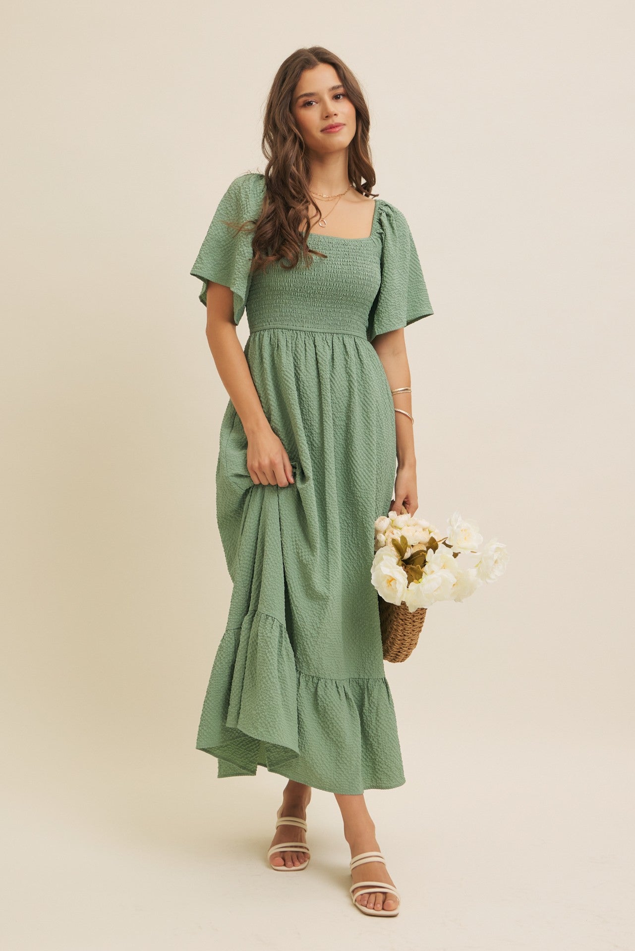 woman wearing a green puff sleeve maxi dress with a smocked bodice and ruffle hem, holding a bouquet of flowers