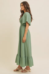 woman wearing a green midi dress with short flutter sleeves and a ruffled hem, posing in profile against a neutral background