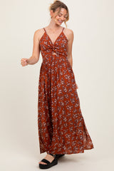woman wearing a rust floral print maxi dress with a knotted front and spaghetti straps, standing and smiling