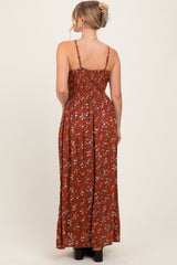 woman wearing a back view of a rust-colored floral maxi dress with adjustable straps and a smocked bodice