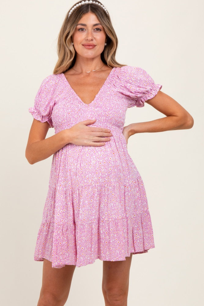 woman wearing a pink floral maternity dress with puff sleeves and a tiered skirt, gently holding her baby bump
