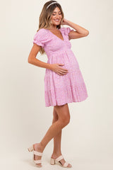 woman wearing a pink floral maternity dress with puff sleeves and holding her baby bump.