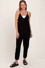 woman wearing a black sleeveless jumpsuit with pockets and adjustable straps, standing against a neutral background