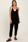 woman wearing a black sleeveless jumpsuit with pockets and adjustable straps, standing against a neutral background