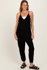 woman wearing a black sleeveless jumpsuit with pockets and tapered legs, styled with a white tank top and black sandals