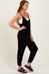 woman wearing a black sleeveless jumpsuit with pockets and a white camisole underneath, styled with black sandals