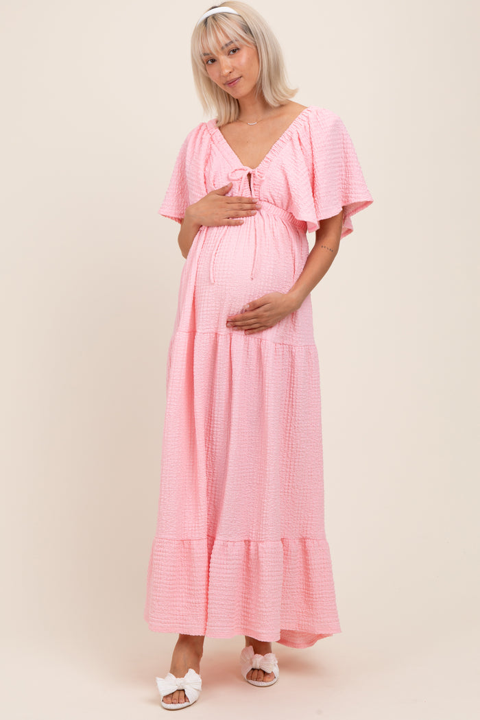 woman wearing a pink short sleeve maternity dress with a tie front and holding her baby bump