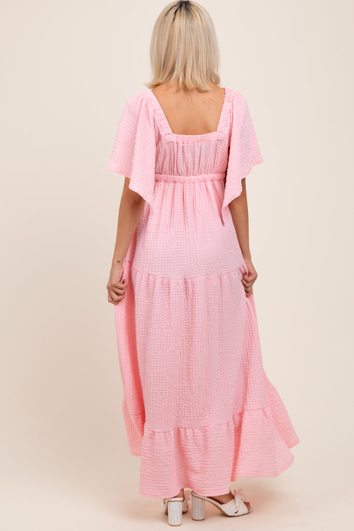 woman wearing a pink short sleeve maternity maxi dress with ruffled sleeves and tiered hem, showing a relaxed fit