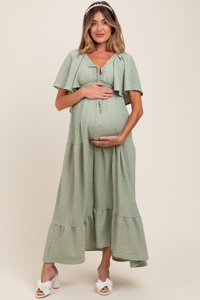 woman wearing a green tiered maxi maternity dress and holding her baby bump