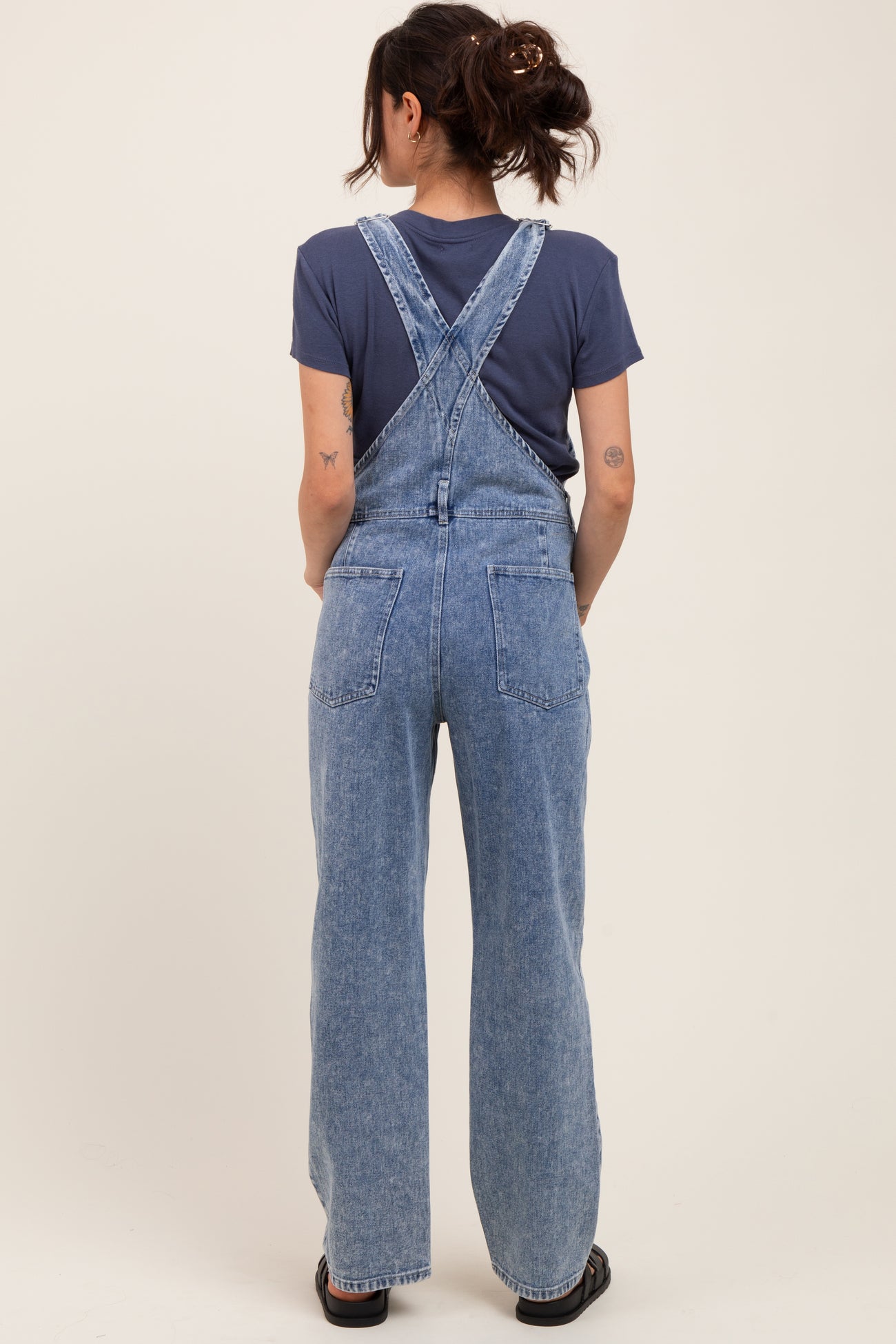 woman wearing light blue maternity denim overalls with a relaxed fit, seen from the back