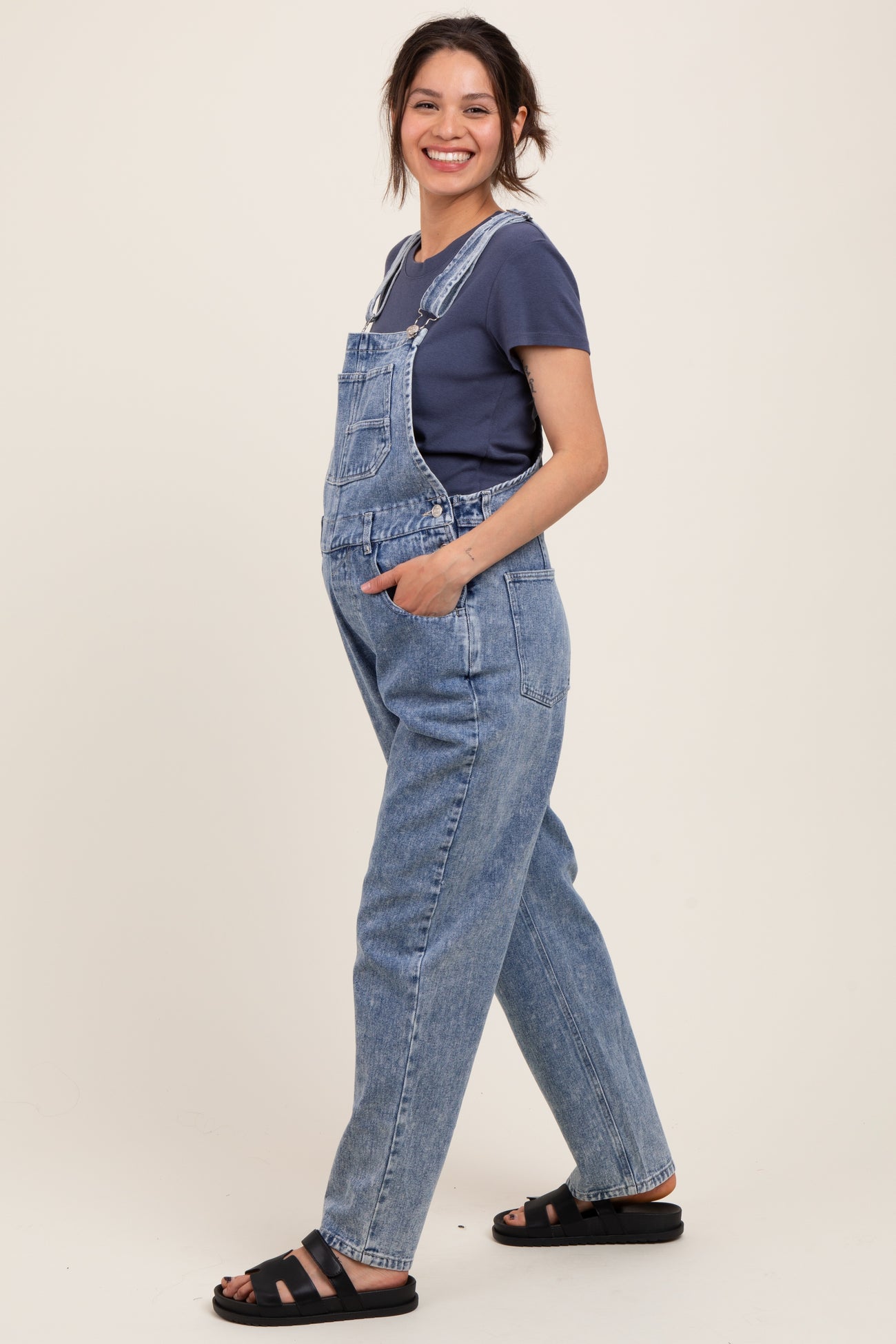 woman wearing a navy t-shirt and light blue maternity overalls, standing with a relaxed pose