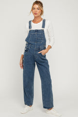 woman wearing a pair of blue denim maternity overalls with a white long sleeve top and sneakers