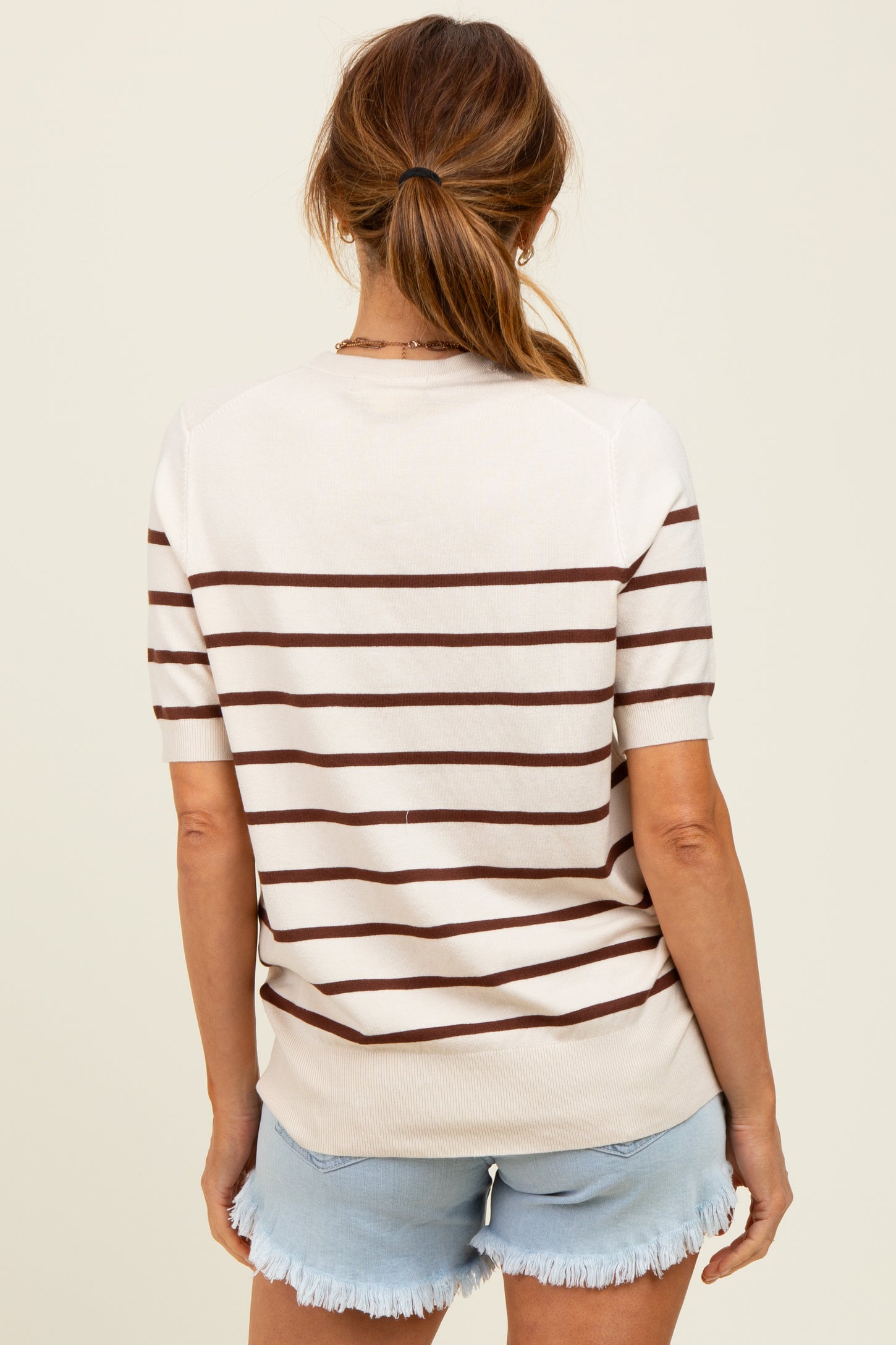 woman wearing a cream and brown striped short sleeve sweater with a relaxed fit and styled with denim shorts