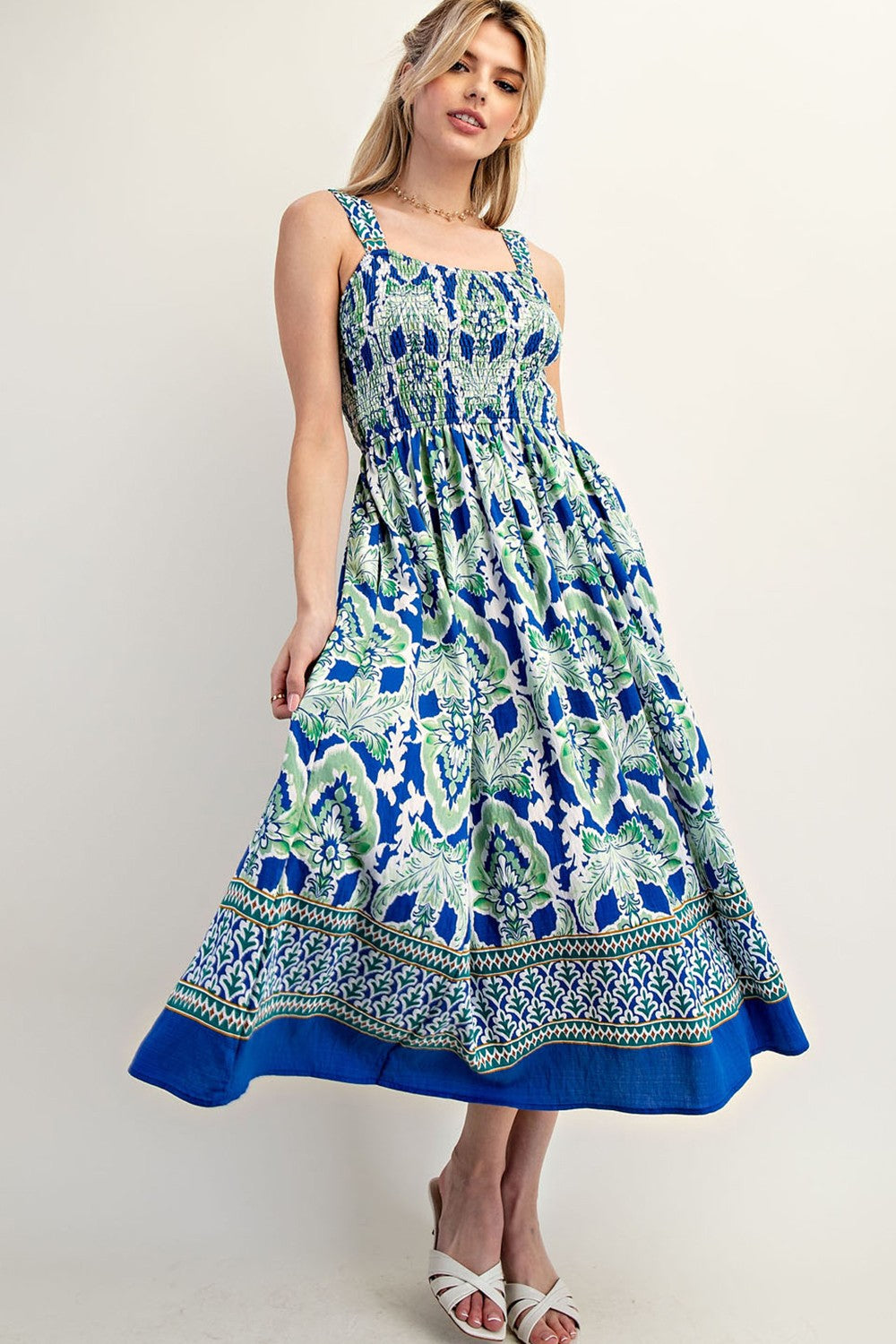 woman wearing a blue and green floral maxi dress with square neckline and smocked bodice, standing in a relaxed pose
