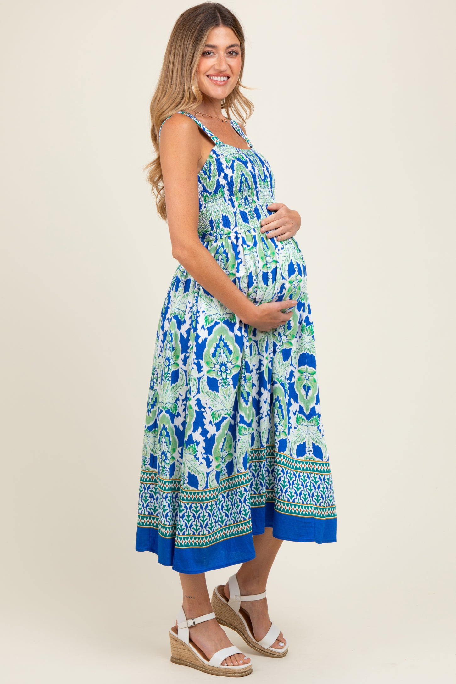 woman wearing a colorful patterned maternity dress with a baby bump, standing and smiling