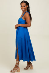 woman wearing a vibrant blue maxi dress with ruffled straps and a thigh slit, standing on a light background