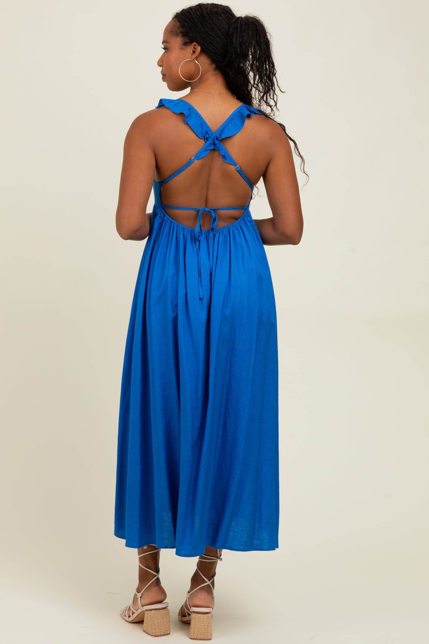 woman wearing a bright blue sleeveless maxi dress with a tied back and open back detail