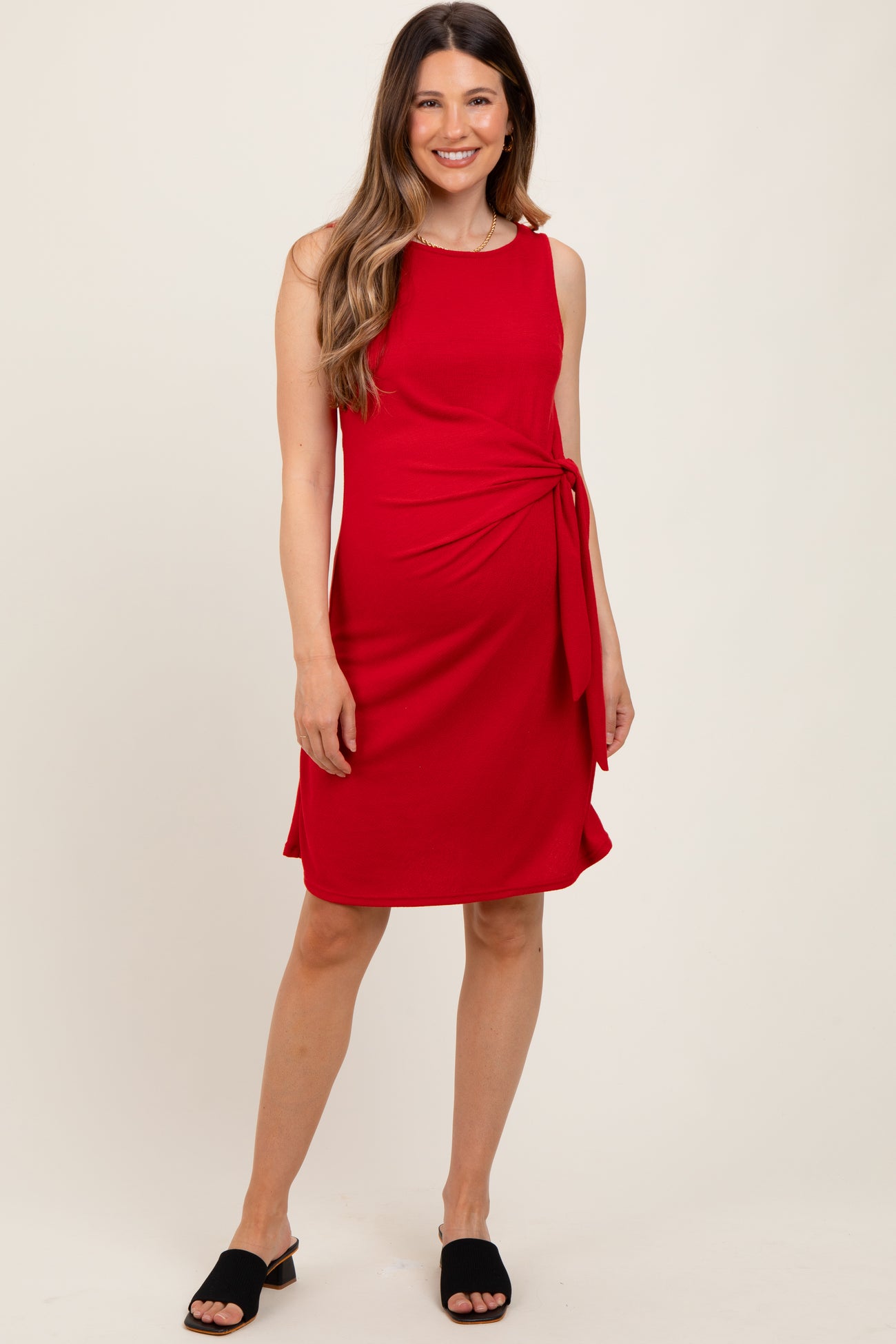 woman wearing a red maternity dress with a side tie detail and a flattering silhouette, styled with black sandals