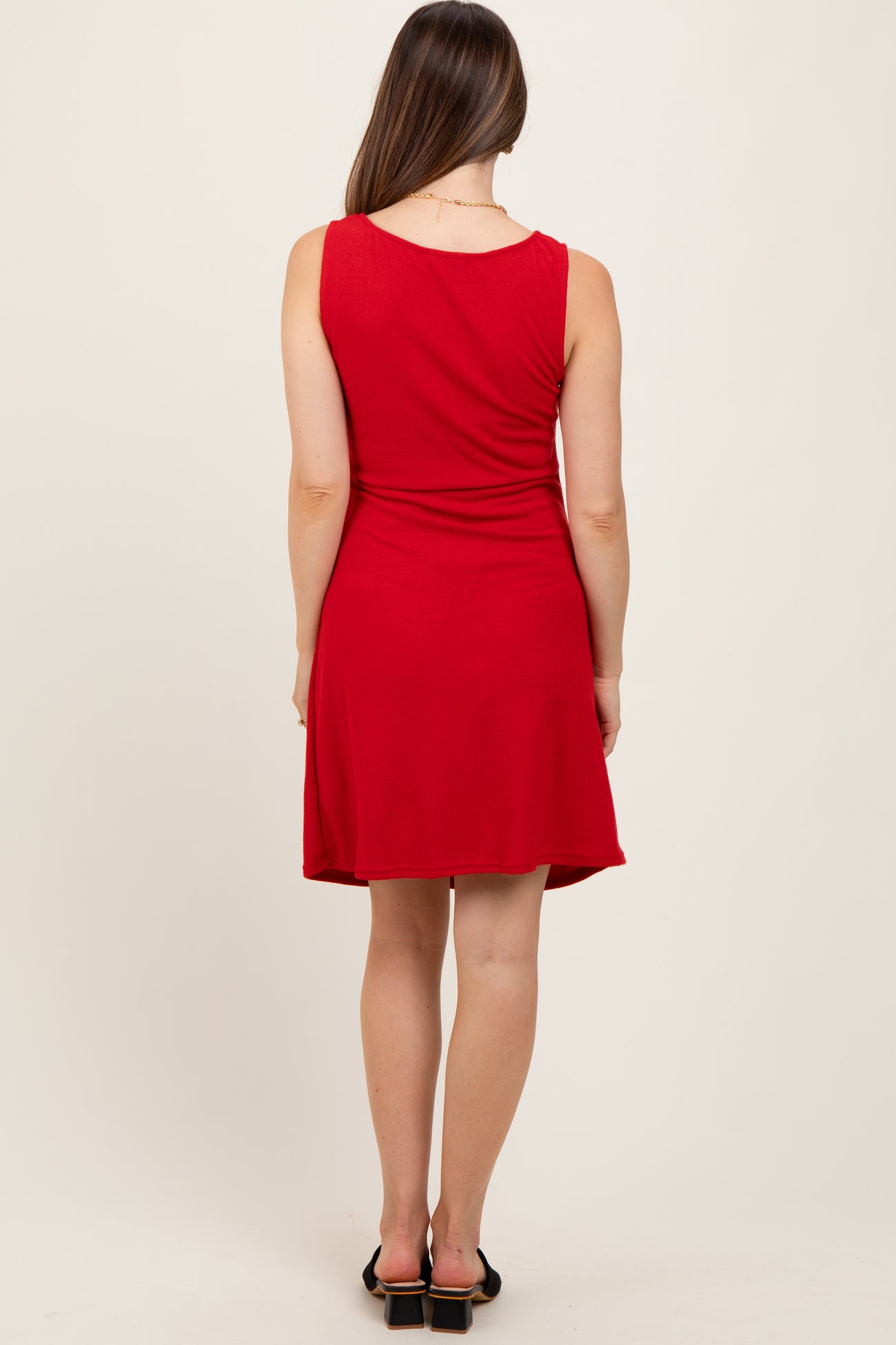 woman wearing a red sleeveless maternity dress with a flared skirt, seen from the back