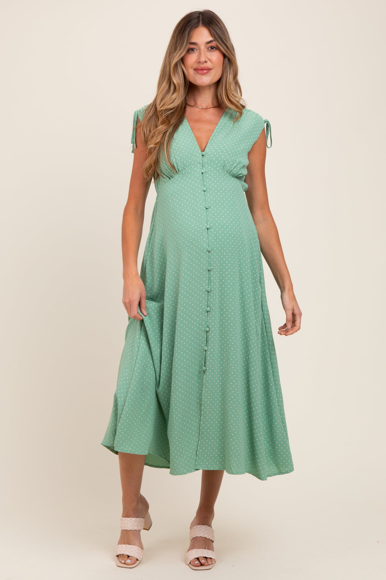 woman wearing a sage green maternity maxi dress with polka dots, a v-neckline, and tie straps, showcasing her baby bump