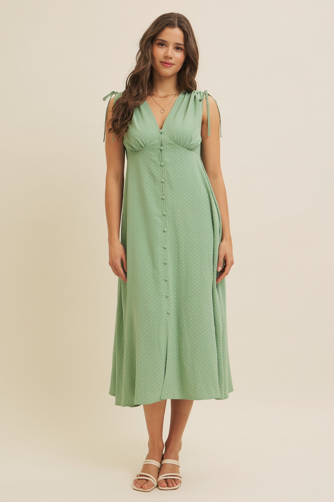 woman wearing a light green midi dress with tie straps and button details on the front