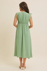 woman wearing a green midi dress with short sleeves and tie details at the shoulders, viewed from the back