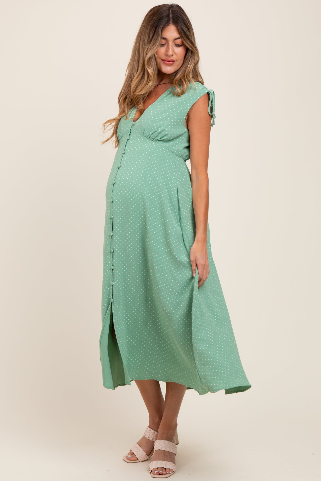 woman wearing a green dotted maternity dress with short sleeves and a button-down front, showcasing her baby bump