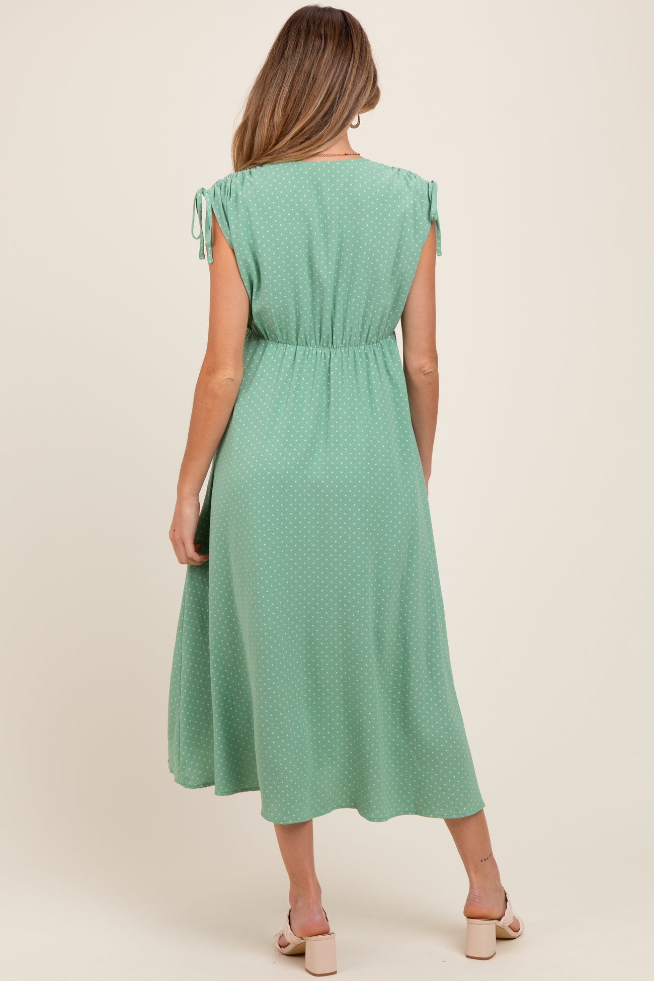 woman wearing a mint green polka dot maternity dress with tie sleeve details and an elastic waist, viewed from the back