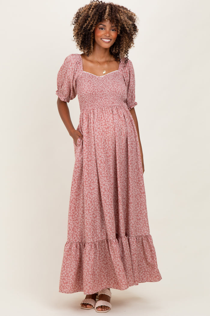 woman wearing a pink floral maternity maxi dress with puff sleeves and pockets, displaying her baby bump