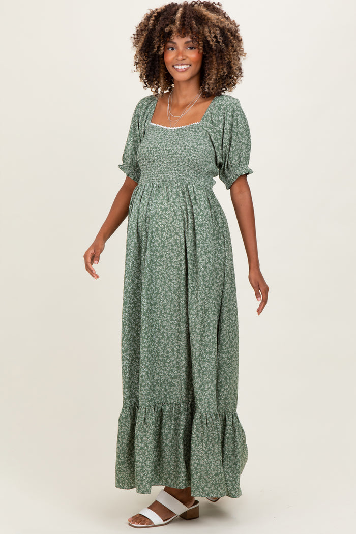 woman wearing a green floral maternity maxi dress with puff sleeves and a ruffled hem, showcasing her baby bump