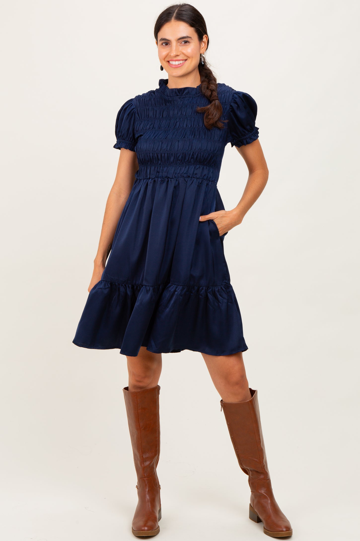woman wearing a navy blue smocked short sleeve dress with pockets, styled with brown knee-high boots