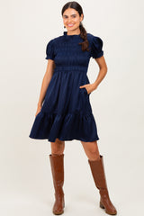 woman wearing a navy blue smocked short sleeve dress with pockets, styled with brown knee-high boots