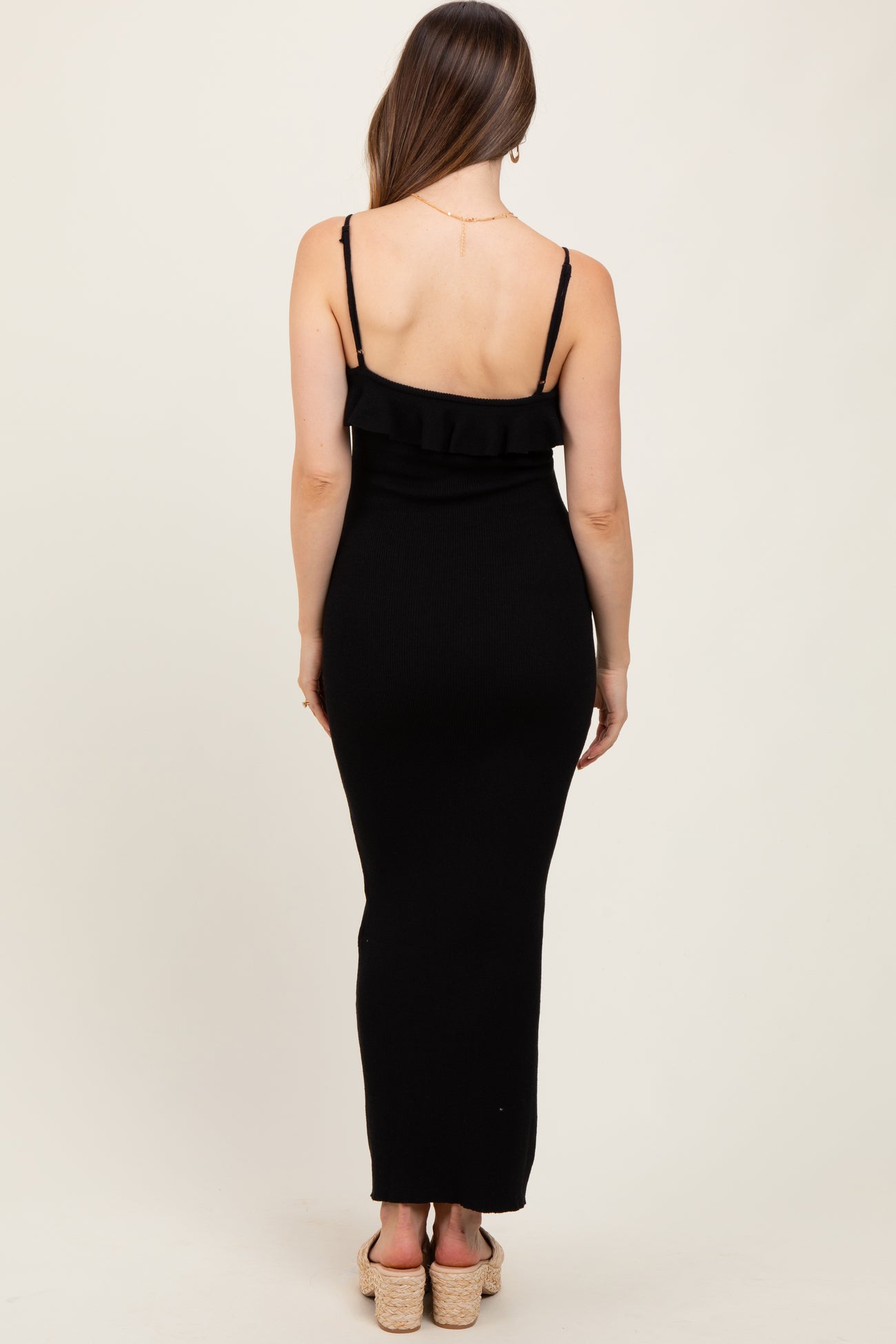 woman wearing a black maternity maxi dress with adjustable straps and ruffle details, showing her back