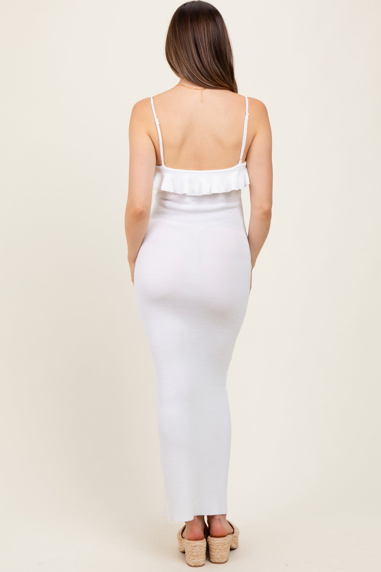 woman wearing a white maternity maxi dress with ruffle detail and spaghetti straps, showcasing a baby bump