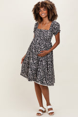 woman wearing a black floral maternity dress with a square neckline and short sleeves, holding her baby bump