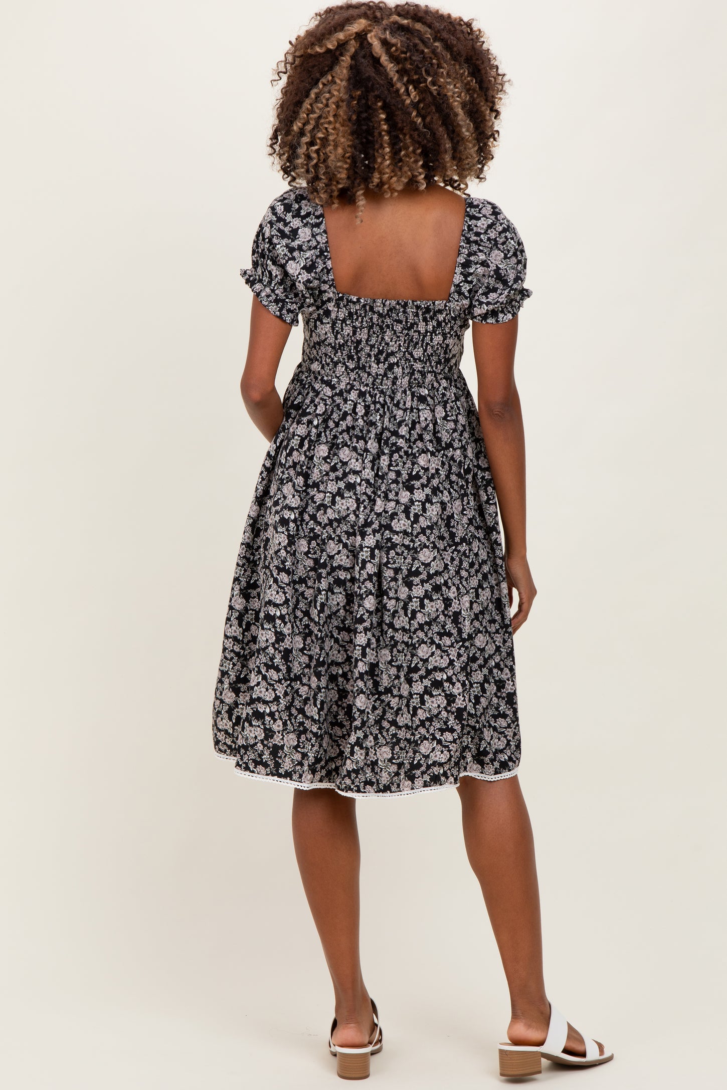woman wearing a black floral maternity dress with short puff sleeves and a smocked back, showing her baby bump